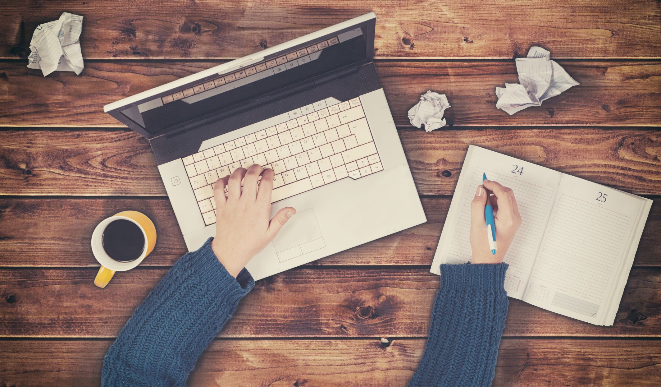 Young person researching for job interview on laptop, with scrunched up paper and coffee next to them.
