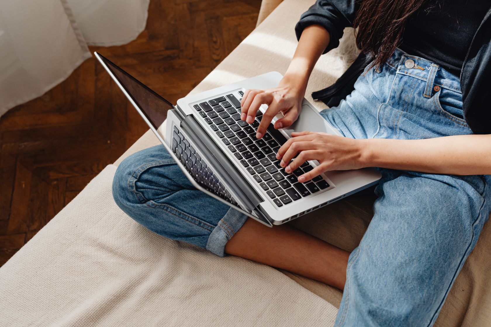 Young person typing cover letter on laptop, sitting on bed